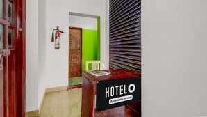 Una reception di hotel con un cartello che riporta 'HOTELO Company-Serviced', un estintore, una porta in legno e una parete verde.