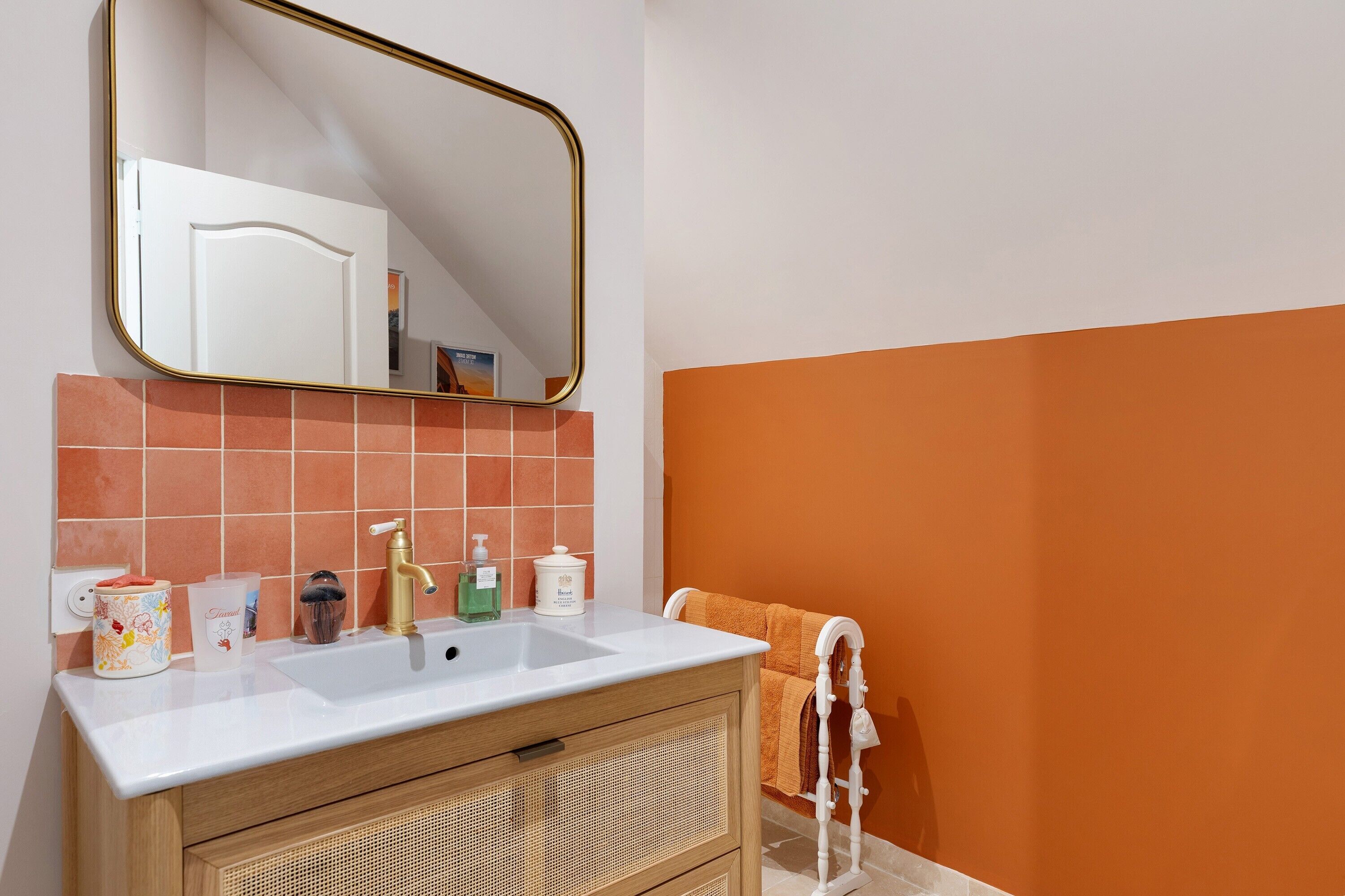 Une salle de bain avec un lavabo blanc, un robinet doré, un miroir avec un cadre doré et un porte-serviettes sur lequel est posée une serviette blanche.