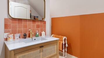 Une salle de bain avec un lavabo blanc, un robinet doré, un miroir avec un cadre doré et un porte-serviettes sur lequel est posée une serviette blanche.