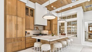 A modern kitchen with wooden cabinets, a marble island, and pendant lighting. - Ciao Bella 721 COA (Port Aransas)
