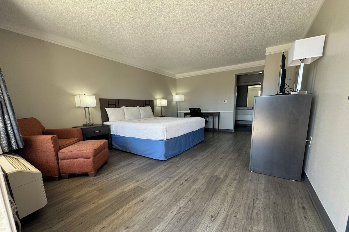 Una habitación de hotel con cama, escritorio, silla, lámpara y refrigerador.
