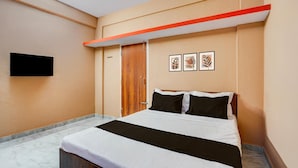 A hotel room with a bed, a flat-screen TV, a wooden door, and two framed pictures on the wall. - Hotel O Bidadi Railway Junction (Ramanagara)
