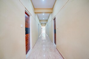 A long, narrow hallway with wooden doors on both sides, a marble floor, and a ceiling with recessed lighting.