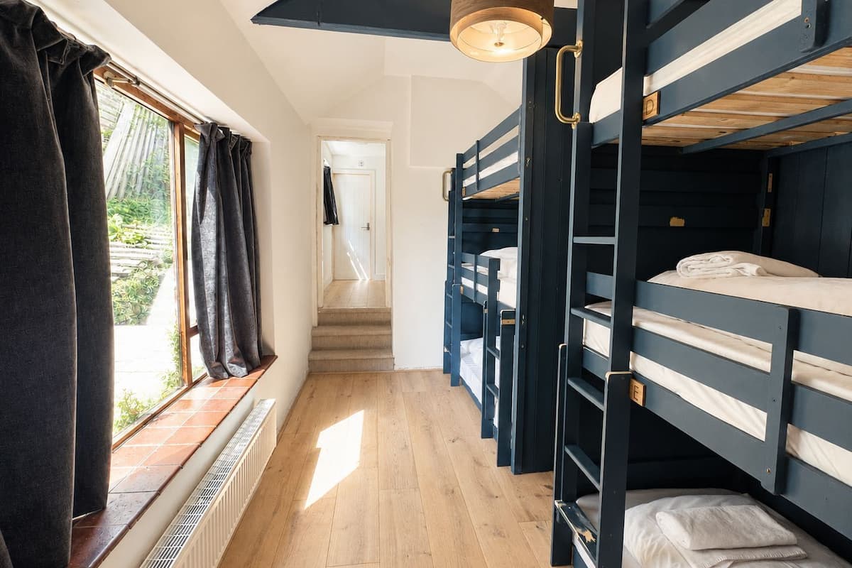 Habitación con literas, una ventana, un radiador y una escalera que lleva a otra habitación.