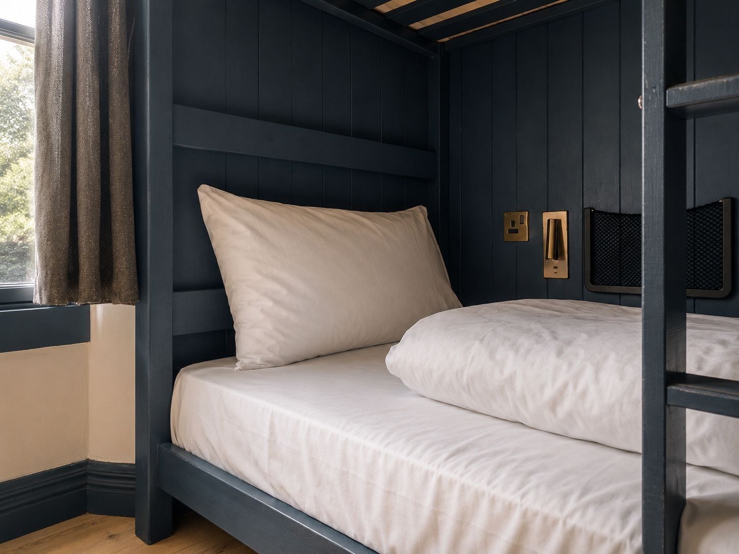 A bunk bed with a headboard, a window with curtains, and wall-mounted light fixtures.