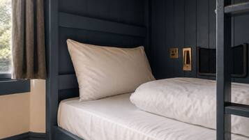 A bunk bed with a headboard, a window with curtains, and wall-mounted light fixtures.