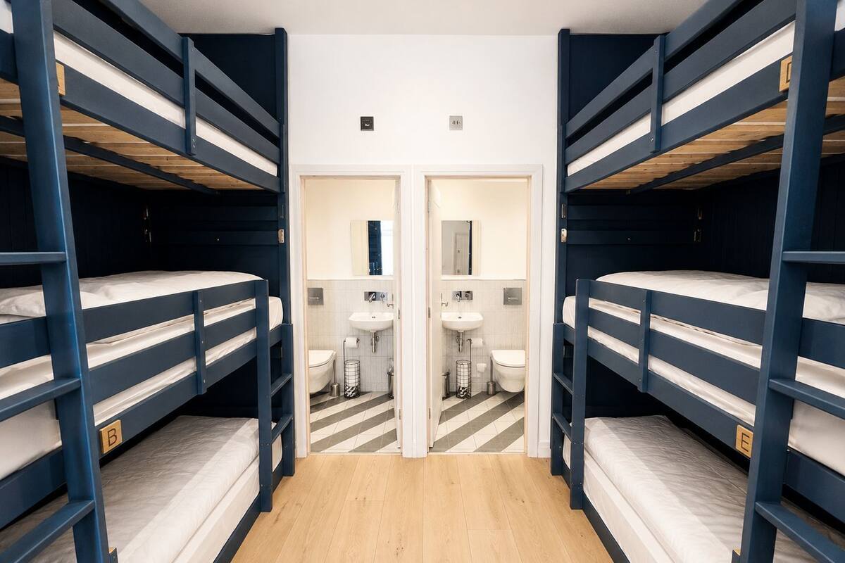 Una habitación con literas, un baño con lavamanos y espejo, y una puerta que da a otra habitación.