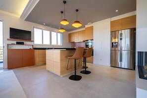 A modern kitchen with a central island, bar stools, a flat-screen TV, and a stainless steel refrigerator. - Penthouse 170m2 with Jacuzzi (La Teste-de-Buch)