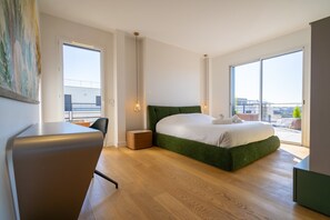 Ein modernes Schlafzimmer mit einem grünen, gepolsterten Bett, einem Holztisch und einem großen Fenster mit Blick auf die Stadt.