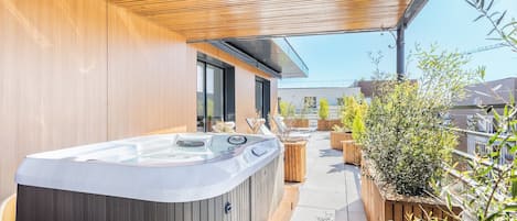 Un bain à remous sous une pergola en bois, sur une terrasse en toit, agrémentée de plantes en pot et offrant une vue sur les bâtiments.