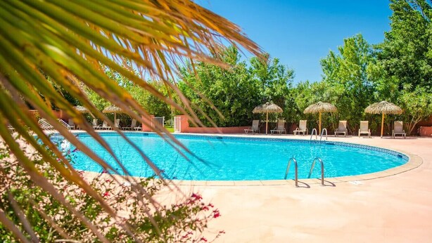 A swimming pool with lounge chairs and umbrellas, surrounded by greenery. - Mobil-home tout confort Camping de l’Escale C43 terrasse, piscine & plages (Agde)