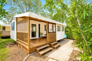 A mobile home with a porch, wooden steps, and a fenced area. - Mobil-home tout confort Camping de l’Escale C43 terrasse, piscine & plages (Agde)