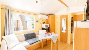 A compact living space with a sofa, a dining table, a microwave, and a television. - Mobil-home tout confort Camping de l’Escale C43 terrasse, piscine & plages (Agde)