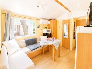 A compact living space with a sofa, a dining table, a microwave, and a television. - Mobil-home tout confort Camping de l’Escale C43 terrasse, piscine & plages (Agde)