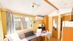 A compact living space with a sofa, a dining table, a microwave, and a refrigerator. - Mobil-home tout confort Camping de l’Escale C43 terrasse, piscine & plages (Agde)