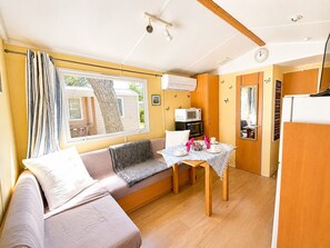 A compact living space with a sofa, a dining table, a microwave, and a refrigerator. - Mobil-home tout confort Camping de l’Escale C43 terrasse, piscine & plages (Agde)