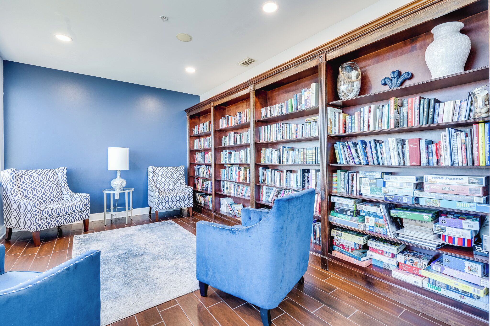 Una biblioteca con estanterías, dos sillones estampados, una lámpara blanca y un sillón azul.