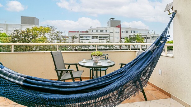 Un hamac sur un balcon, avec une table et des chaises, une plante en pot et une vue sur les bâtiments.