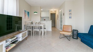 Un salon avec un téléviseur, un coin repas, un canapé bleu et une cuisine à l’arrière-plan.