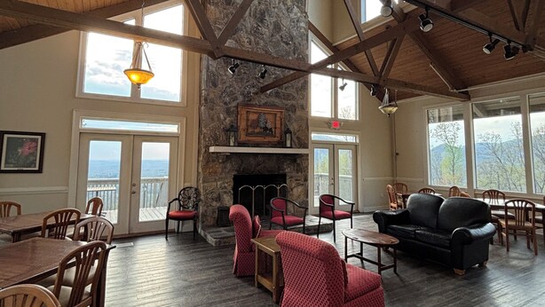A spacious room with a stone fireplace, wooden beams, and large windows. - Bent Tree Family 2BR - Hot Tub, Mountain View Deck, Pool, Golf, Lake & Fish (Jasper)