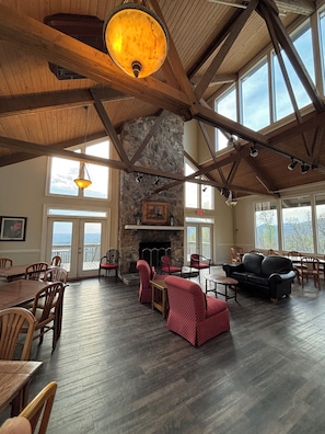 A spacious room with a stone fireplace, wooden beams, and large windows.