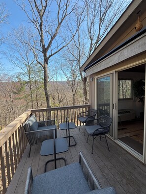 A wooden deck with outdoor furniture, a glass door leading inside, and a view of trees and hills. - Bent Tree Family 2BR - Hot Tub, Mountain View Deck, Pool, Golf, Lake & Fish (Jasper)