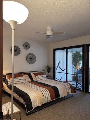 A bedroom with a bed, a ceiling fan, wall art, and a view through a sliding door.