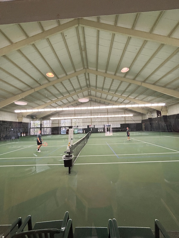 An indoor tennis court with a high ceiling, a net, and a few players.