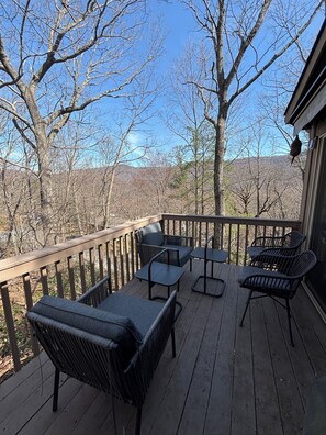 A wooden deck with outdoor furniture, a railing, and a view of trees and hills.