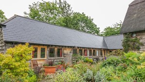 Ein rustikales Holzgebäude mit geneigtem Dach, umgeben von einem üppigen Garten mit verschiedenen Pflanzen und Blumen.
