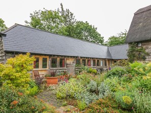 A rustic wooden building with a sloped roof, surrounded by a lush garden with various plants and flowers. - Ryepiece (Stratford-upon-Avon)