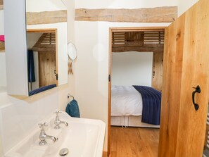 Quarto compacto com teto de madeira, uma cama de solteiro com cobertor azul e uma pia branca com espelho.
