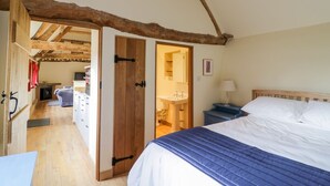 Ein Schlafzimmer mit Holzboden, einem Bett mit blauer und weißer Bettdecke, einem Nachttisch mit Lampe und einem durch eine offene Tür einsehbaren Badezimmer.