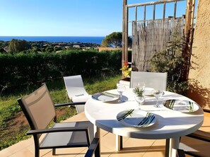 A round outdoor table with white chairs, set for dining, overlooking a scenic landscape with a view of the sea and greenery. - Air-conditioned Studio 'Sant Ambrogggio' – Terrace with Sea View and Sunset (Lumio)