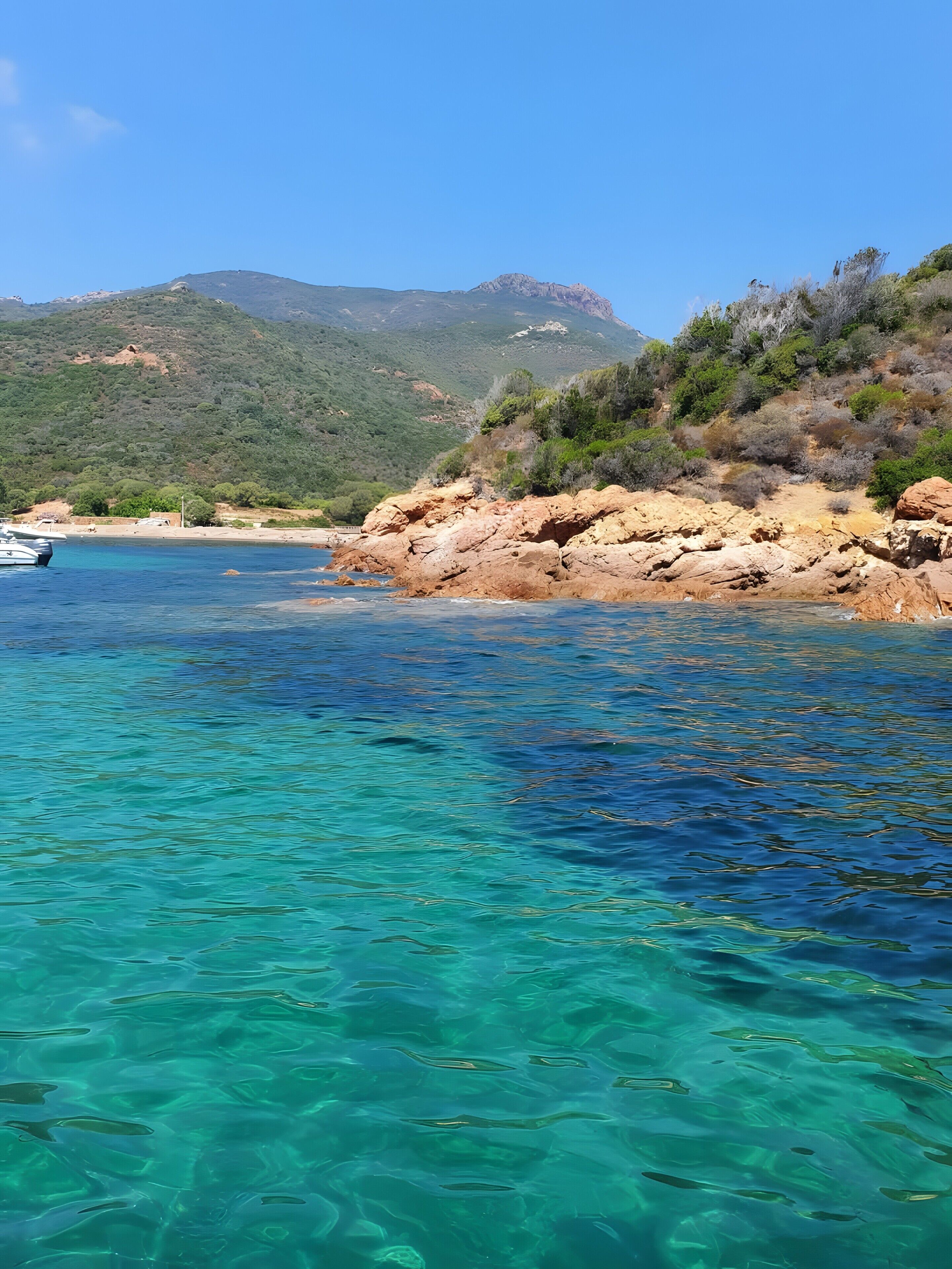 Kustgebied met helder turquoise water, rotsachtig terrein en een bergachtige achtergrond.