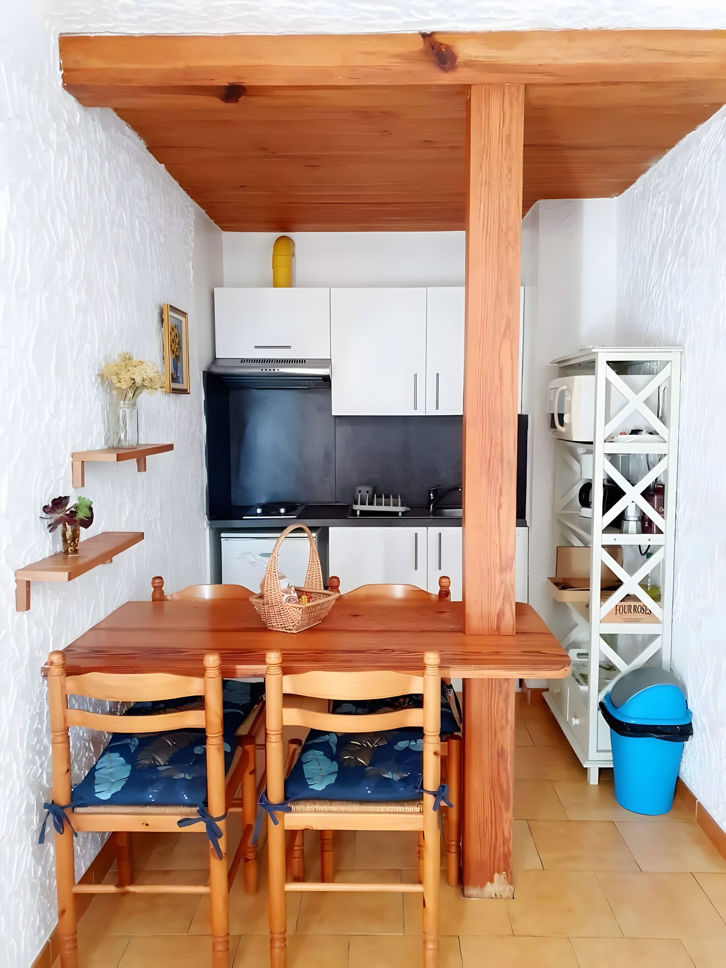 Une cuisine compacte avec des meubles blancs, une cuisinière noire et une table à manger en bois, accompagnée de chaises.