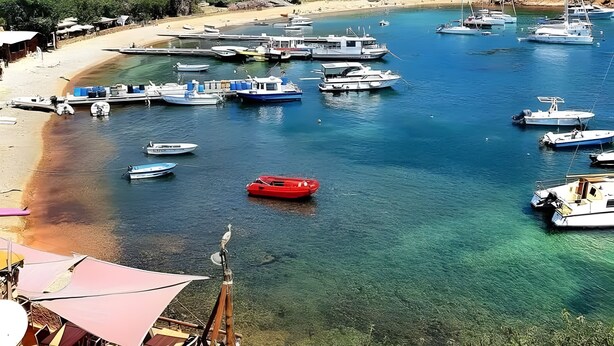 A coastal marina with boats docked, a beach, and mountains in the background. - Air-conditioned Studio 'Sant Ambrogggio' – Terrace with Sea View and Sunset (Lumio)