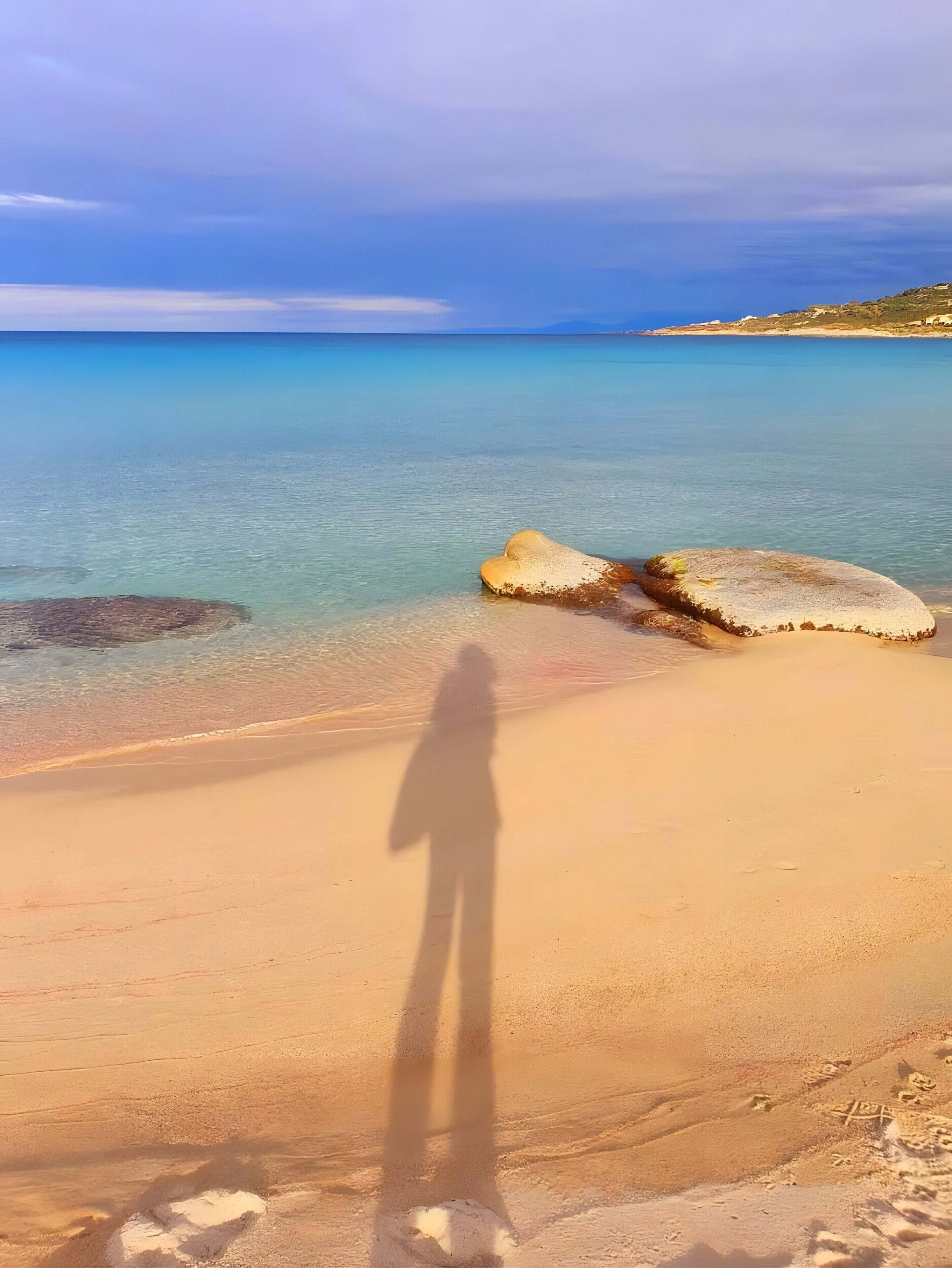 Une plage à l’eau claire, la silhouette d’une personne et une côte lointaine.