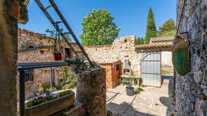Un patio de piedra con una escalera de madera, plantas en macetas y un edificio rústico con techo de tejas.