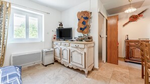 Una habitación con un radiador blanco, un televisor en un mueble, una puerta de madera y una ventana con cortinas.