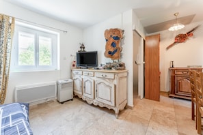 A room with a white radiator, a TV on a cabinet, a wooden door, and a window with curtains.