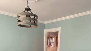 Un comedor con una mesa de madera oscura y sillas blancas tapizadas, una lámpara colgante y vista a la cocina.