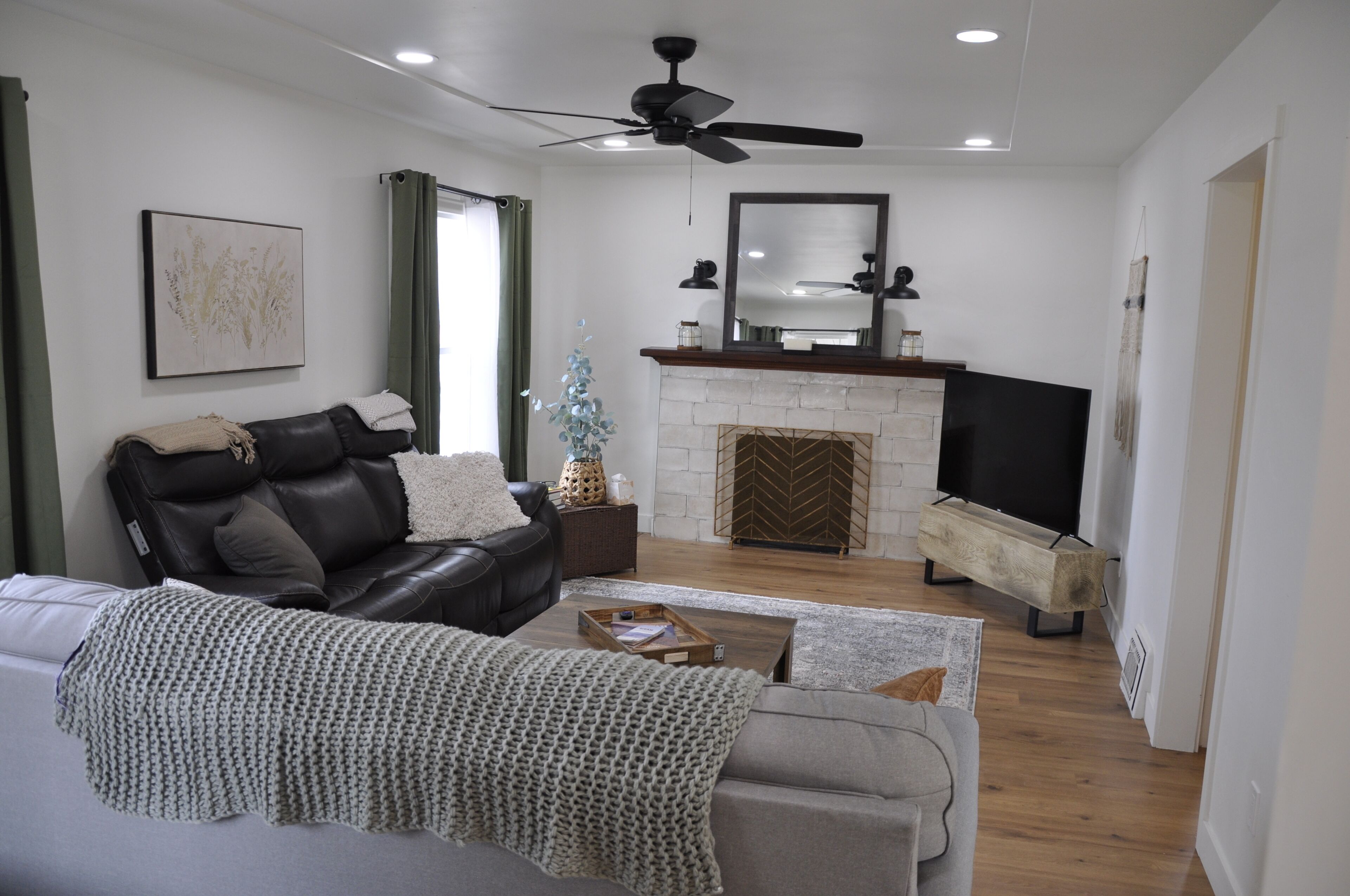 A living room with a sofa, a coffee table, a fireplace, a television, and a ceiling fan.