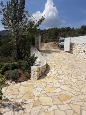 A stone pathway leading to a stone wall with a vehicle parked nearby. - Villa venetia (Corfu)