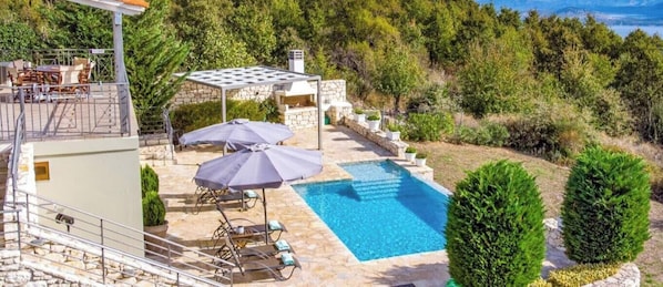 A pool with sun loungers and umbrellas, surrounded by stone walls and greenery. - Villa venetia (Corfu)