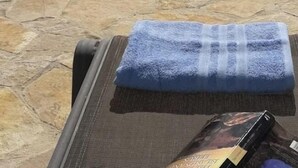 Una piscina con vista sulle montagne e su un lago, un asciugamano e un libro su una sedia.