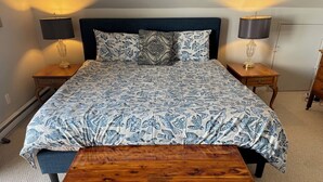 Un dormitorio con una cama, dos mesitas de noche, un banco de madera y dos lámparas.