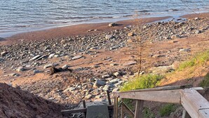 Una escalera de madera que desciende hacia una playa rocosa con vista al mar.