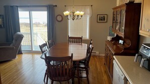 Un comedor con una mesa y sillas de madera, una lámpara de araña, una cocina con lavavajillas y vistas a través de una puerta corrediza de vidrio.