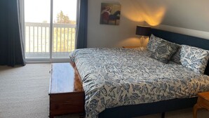 Un dormitorio con cama, mesita de noche, lámpara, un cuadro y vistas al exterior.